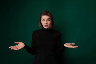 Siyah gömlek giyen bir kadın iki elini de dışarı doğru uzatıyor. Elleri hafifçe kavrulmuş, tarafsız bir pozisyonda duruyor gibi görünüyor. Yüz ifadesi tarafsız..
