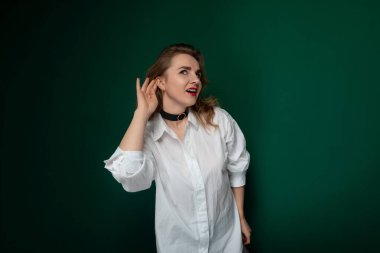 Çerçevede beyaz gömlek giyen ve boynunda siyah bir boyunluk olan bir kadın görülüyor. Kıyafeti sade ama şık. Renkleri de çok farklı. Biraz da sofistike.