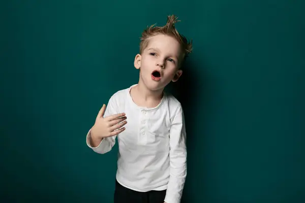 Stock image A young boy is seen standing upright against a vibrant green wall. His posture is confident as he gazes towards the viewer. The wall provides a stark backdrop, emphasizing the boys presence in the