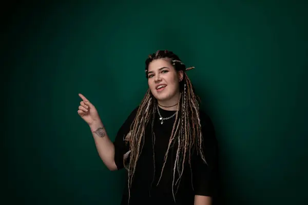 stock image A woman with dreadlocks is pointing at something off-camera. She appears to be engaging in a conversation or directing attention towards a specific object. Her facial expression indicates focus and