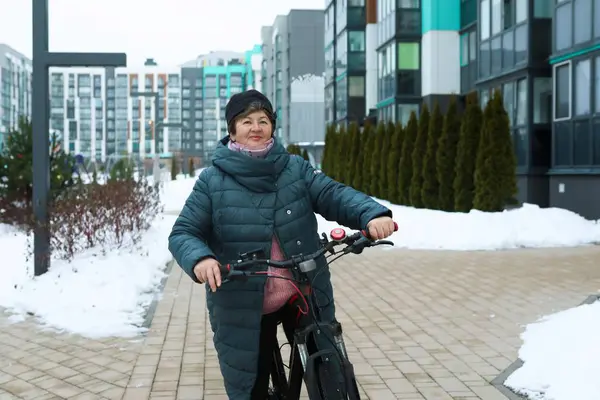 An elderly woman rides on a bike path in winter.