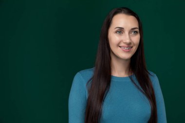 Mavi bluz giyen bir kadın doğrudan kameraya gülümsüyor. Yüzü neşeli ve misafirperver..