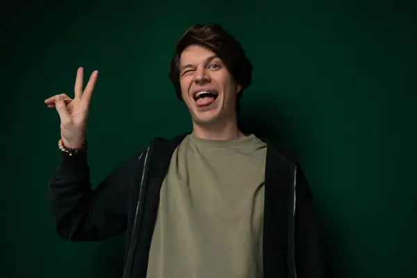 stock image A man is extending his index and middle fingers to form a peace sign gesture with his hand against a neutral background.