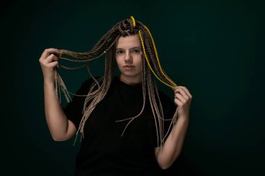 Kafasında rasta olan bir kadın ayakta kameraya bakıyor. Sırtından dökülen uzun, kıvırcık saçları var. Rasta desenleri düzgünce tasarlanmış ve eşsiz saç dokusunu gösteriyor..