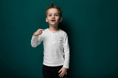 Genç bir çocuk canlı yeşil bir duvarın önünde duruyor, dümdüz ileriye bakıyor. Meraklı ve çevresiyle meşgul görünüyor..