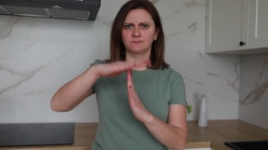 Omuz hizasında saçları olan, sıradan yeşil tişört giyen genç bir kadın mermer kaplamalı çağdaş bir mutfakta duruyor. Onu büyütürken şaşkınlık ifadesi sergiliyor.