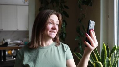 Bir kadın cep telefonu kamerasıyla kendi portresini çekiyor. O, resme poz vermek için telefonu kol mesafesinde tutuyor. Kamera panjurunun sesi duyulabilir..