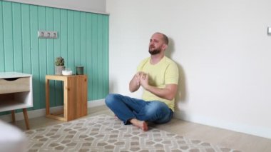 Huzurlu bir adam soluk bir duvara bağdaş kurup gündüz saatlerinde minimalist oturma odasının huzurlu ortamında meditasyon yapıyor..