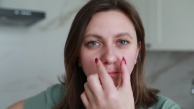 Sıradan yeşil tişörtlü odaklanmış genç bir kadın titizlikle tırnaklarına kırmızı oje sürüyor, kendi evinde kendine bakım yapıyor..