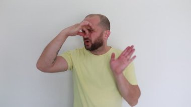 Sıradan sarı tişört giymiş kel bir adam saf beyaz bir arkaplana karşı duruyor, karmaşadan sürprize çeşitli duygular ifade ediyor, ve ara sıra elleriyle işaret ediyor.