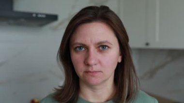 Bir kadın mutfakta şaşkın ve biraz hayal kırıklığına uğramış bir ifadeyle duruyor. Gün ışığı odayı aydınlatıyor, özelliklerini ve arkasındaki mutfağı aydınlatıyor..