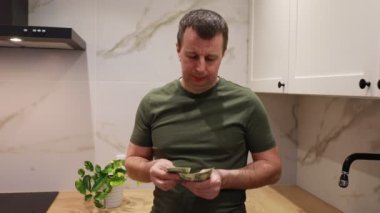 Yeşil tişörtlü bir adam mutfak lavabosunda ellerini sabun ve suyla parlak bir mermer tezgahla yıkıyor. Ev ortamında temizlik sağlamak için görevine odaklanıyor..