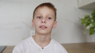 Çarpıcı mavi gözlü genç bir çocuk, arka planda hafif bir kapalı bitki ile süslenmiş parlak ışıklı bir odada, düşünceli bir yüz ifadesiyle yukarıya bakarken yakalanır.