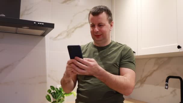 Man Standing Kitchen Fixated His Cell Phone Screen Appears Engaged — Wideo stockowe