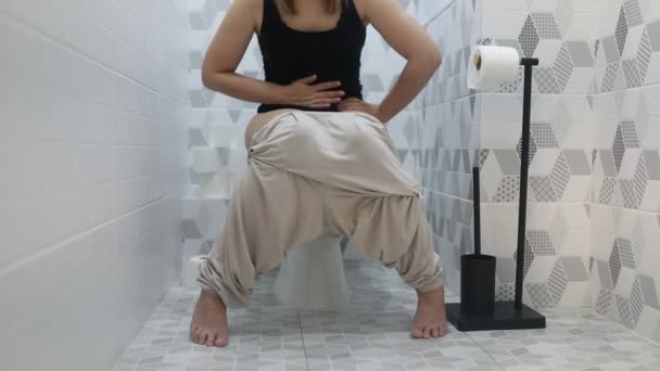 视频中一个女人坐在浴室的马桶上 这名妇女正在使用厕所 似乎是在一个私密的环境中 重点完全放在坐在马桶上的动作上 — 图库视频影像