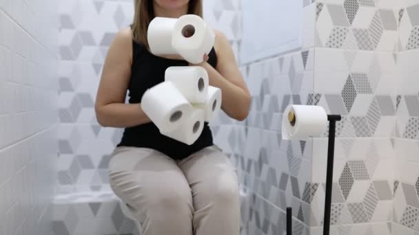 女性がトイレの座席に座り 手元にトイレットペーパーを2本置いている 彼女はトイレの設定で屋内にあるように見えます — ストック動画