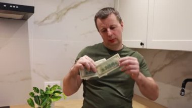 Yeşil gömlek giyen bir adam elinde iki banknot tutarken görülüyor. Faturalar para birimlerine ait gibi görünüyor. Erkeğin ifadesi ve çevresi belirtilmemiş..