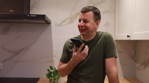 Hombre Está Pie Una Cocina Moderna Sosteniendo Hablando Teléfono Inteligente — Vídeo de stock