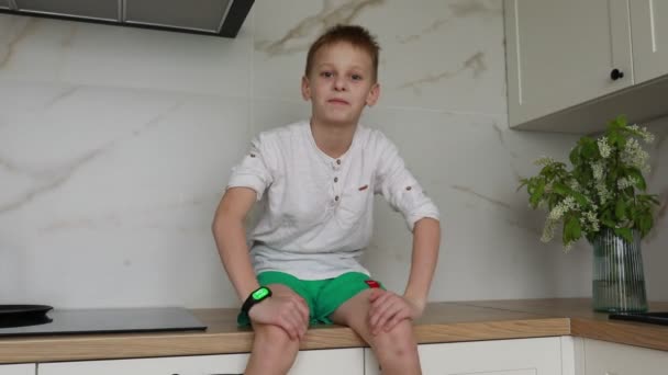Młody Chłopiec Siedzi Blacie Kuchennym Prawdopodobnie Czekając Posiłek Lub Pomagając — Wideo stockowe