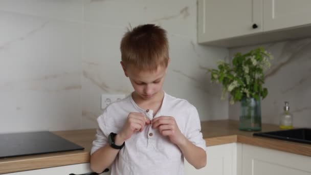 一个注意力集中的小男孩正在学习如何在一个阳光灿烂的现代化厨房里把衬衫扣上纽扣 他的小手指灵巧地紧紧抓住每一个纽扣孔 这标志着在发展中的一个里程碑 — 图库视频影像