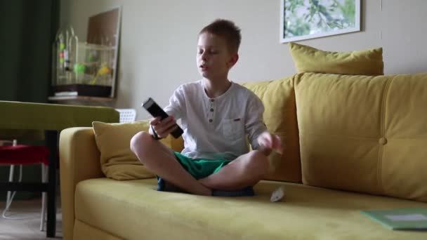 Ein Kleiner Junge Sitzt Drinnen Auf Einer Couch Und Hält — Stockvideo