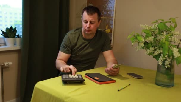 一个专心致志的人 拿着计算器 智能手机和钱包坐在餐桌旁 忙于整理个人财务 在使用其他金融工具的同时 计算器也在被积极使用 — 图库视频影像