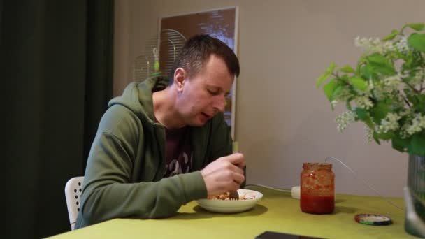 一个男人坐在桌旁吃饭 他在椅子上拿起器皿 边吃边吃 — 图库视频影像