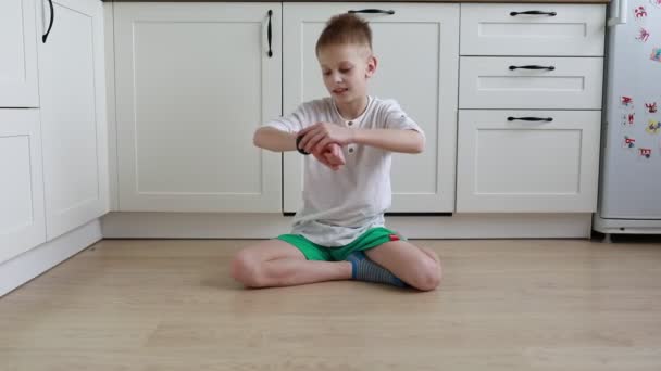 Młody Chłopiec Siedzi Podłodze Kuchni Rozgląda Się Bawi Zabawkami Wygląda — Wideo stockowe