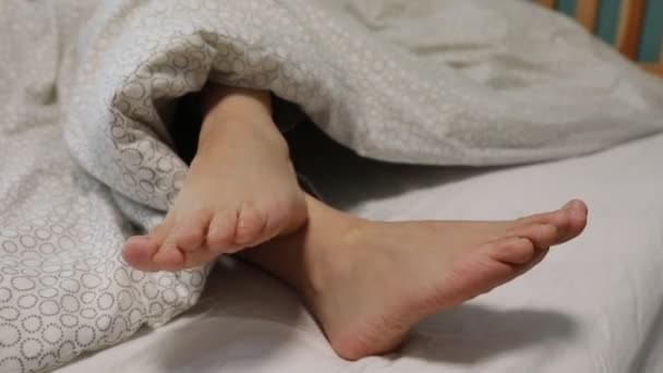 一双赤脚从有花纹的垫子下面伸出来 暗示一个人可以舒服地放松一下 也许可以在舒适的床上过夜 — 图库视频影像