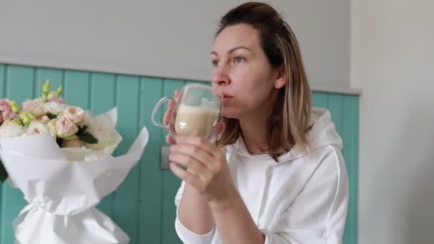 여자가 뜨거운 음료를 마시고 편안하게 실내에 그녀의 신선한 꽃다발과 휴식을 — 비디오