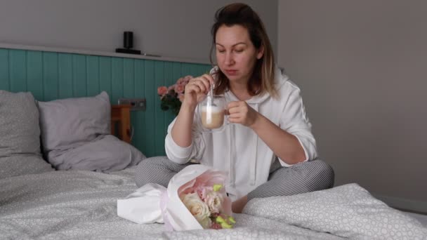 一个女人穿着睡衣在舒适的床上放松下来 在一个安静的周末早晨品尝着新鲜的咖啡和美味的羊角面包 当她放松的时候 缓慢的早晨的悠闲优雅被捕捉了 — 图库视频影像
