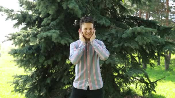 Ένας Χαρούμενος Νεαρός Άνδρας Στέκεται Μπροστά Από Βαθιά Πράσινα Κωνοφόρα — Αρχείο Βίντεο