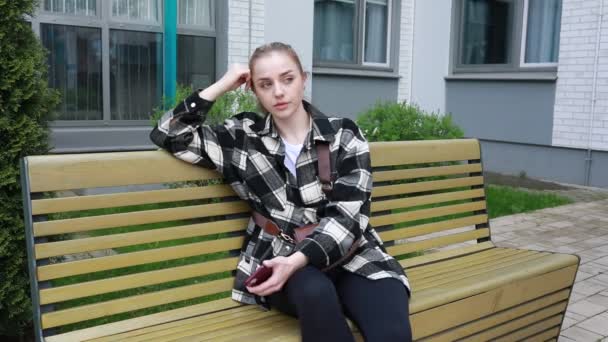 Μια Νεαρή Γυναίκα Στηρίζεται Ένα Ξύλινο Παγκάκι Έξω Από Ένα — Αρχείο Βίντεο