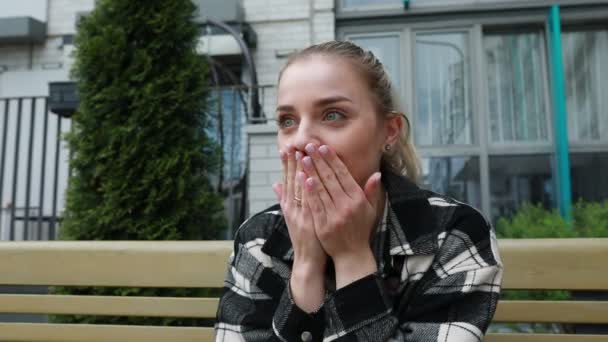Młoda Kobieta Siedzi Ławce Miejskim Otoczeniu Zakrywając Usta Dłońmi Geście — Wideo stockowe