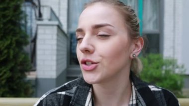 Düşünceli genç bir kadın, düşünceli bir ifadeyle modern bir şehir binasının yanında duruyor. Düşüncelere dalmış ya da birini bekliyor gibi görünüyor..