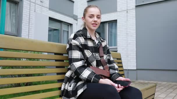 Una Mujer Joven Está Sentada Cómodamente Banco Público Sosteniendo Teléfono — Vídeos de Stock