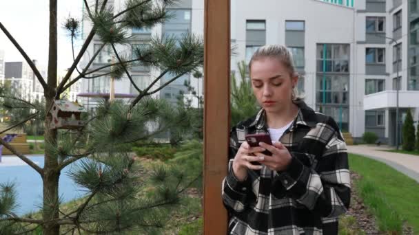 Молода Жінка Стоїть Поруч Сосновим Деревом Міському Парку Зачарованому Смартфоном — стокове відео