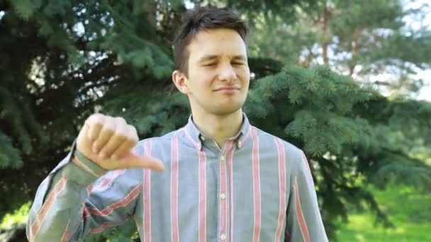 Young Man Stands Outdoors Surrounded Greenery Expressing Disapproval Dissatisfaction Clear — Stock Video