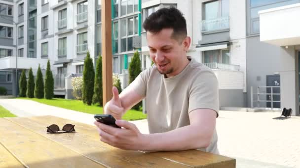 Ein Mann Sitzt Einem Tisch Seinen Handybildschirm Vertieft Wirkt Konzentriert — Stockvideo