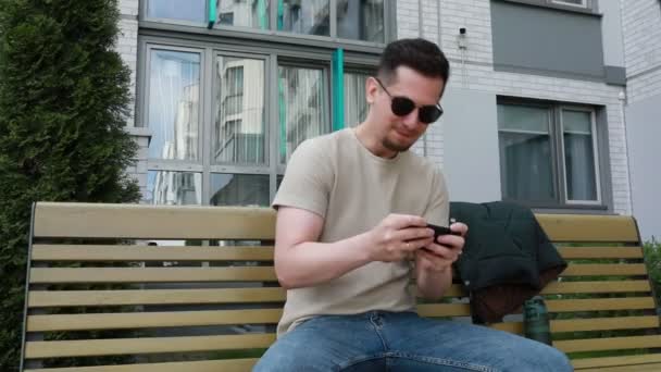 Bir Adam Bankta Otururken Görülüyor Cep Telefonuna Dalmış Aygıt Ekranına — Stok video