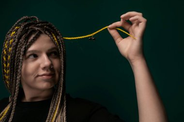 Rasta saçlı bir kadın elinde parlak sarı bir ip tutarken görülüyor. Elinde tuttuğu nesneyle odaklanmış ve meşgul görünüyor..