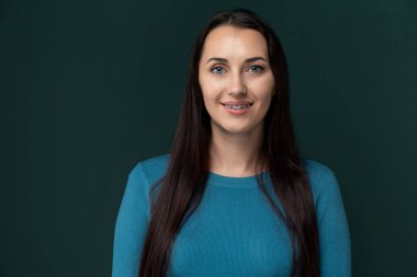 Mavi gömlek giyen bir kadın kameraya gülümsüyor. İzleyiciyle göz teması kurarken mutlu ve arkadaş canlısı görünüyor..