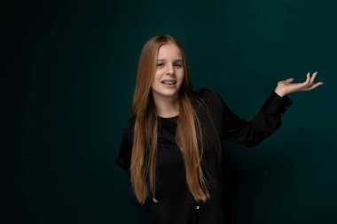 Parlak, uzun kızıl saçlı bir kadın sağlam yeşil bir duvarın önünde duruyor. Onun varlığı dikkat çekiyor. Saçları sırtına doğru dökülüyor, zarif duruşuna doğru gözlerini çekiyor..
