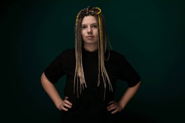 Sarışın, uzun saçlı bir kadın, elleri kalçalarının üzerine sıkıca yerleştirilmiş olarak güvenle ayakta duruyor. Duruşu, önüne bakarken güç ve bağımsızlık yayıyor..