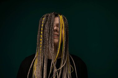 Uzun saçlı bir kadın canlı yeşil bir arka planın önünde kendinden emin bir şekilde duruyor. Saçları sırtına doğru dökülüyor, sert renk arkaplanına çarpıcı bir kontrast oluşturuyor..