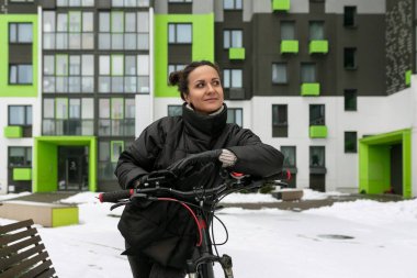 Siyah ceketli güzel bir kadın evinin yanında bisikletle yürüyor..