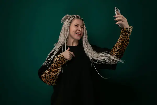 stock image A woman with long white hair is holding a cell phone in her hand. She appears to be focused on the screen, possibly texting or browsing. The background is neutral, placing all attention on the woman