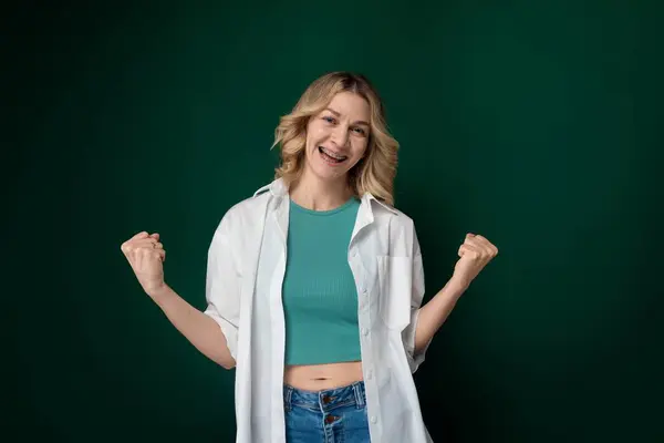 stock image A woman wearing a green shirt and white jacket standing outdoors. She is looking directly at the camera, with a neutral expression on her face.