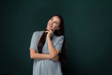 Uzun saçlı bir kadın canlı yeşil bir duvarın önünde duruyor. Saçları sırtına doğru süzülüyor ve görünüşe göre uzaklığa bakıyor..