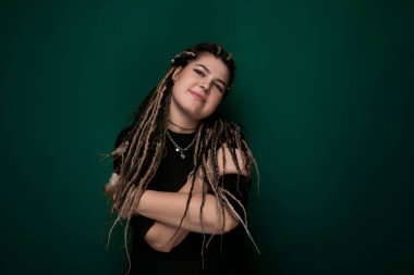 Parlak yeşil bir altyapının önünde kendinden emin bir şekilde duran rastalı bir kadın. Onun ayırt edici saç stili canlı arkaplanda göze çarpar..